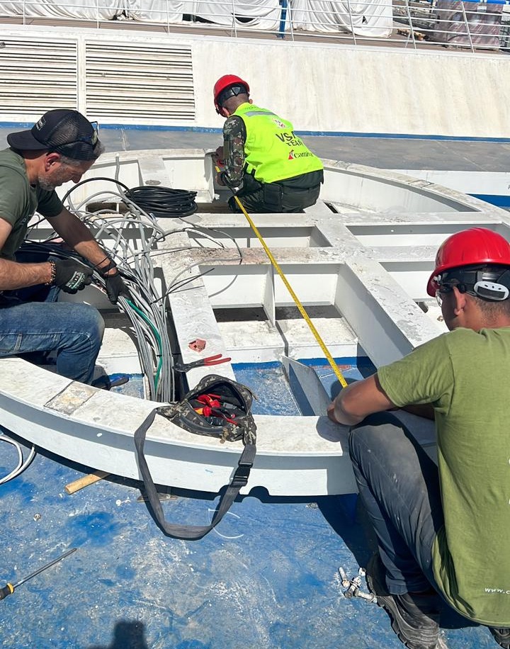 Technicians preparing and installing a heavy-duty structural mount for a VSAT satellite antenna on a ship deck.